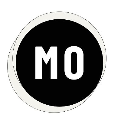 Eine Frau praktiziert Yoga in einem hellen Raum. Sie sitzt im Schneidersitz auf einer Yogamatte und trägt eine weiße Oberbekleidung. Neben ihr steht ein dekorativer Gegenstand.