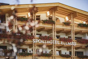 Traditionelles alpines Hotel mit Holzfassade, Blumenkästen und dem Schriftzug "Sporhotel Ellmau" vor einer Berglandschaft.