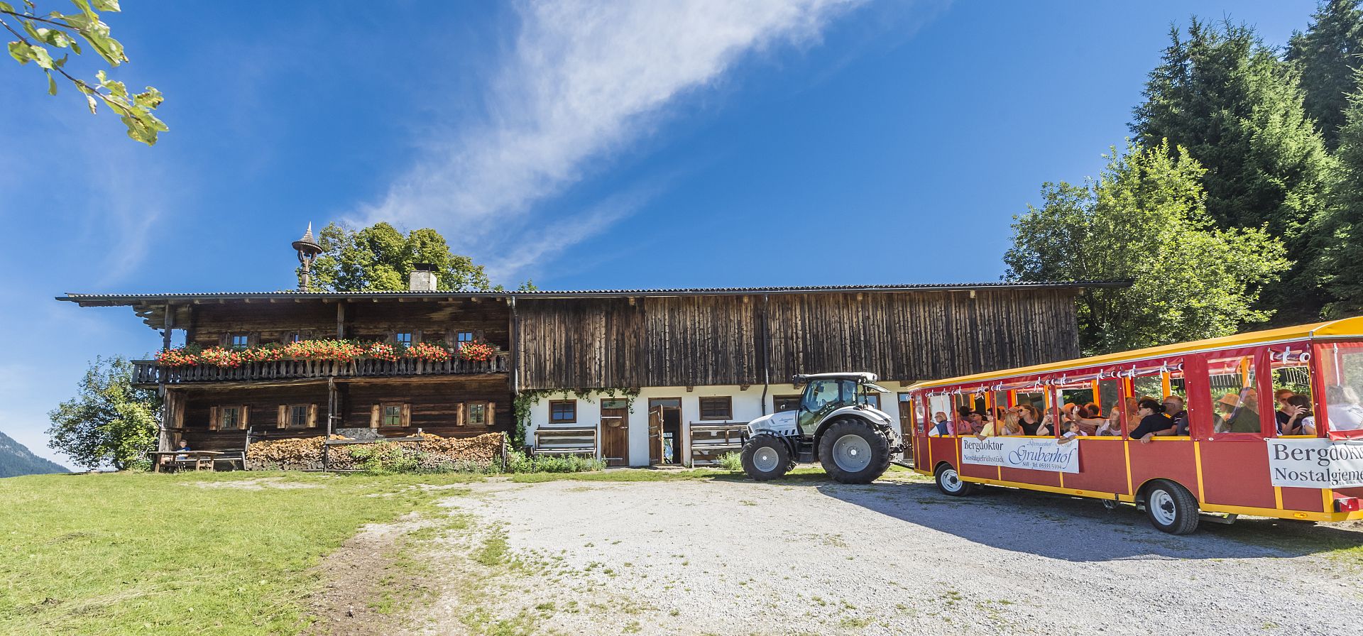Ein rustikales Holzgebäude mit Blumenkästen steht auf einem grünen Hügel. Umgeben von Bäumen und einem Holzzaun, scheint die Szenerie idyllisch und friedlich.