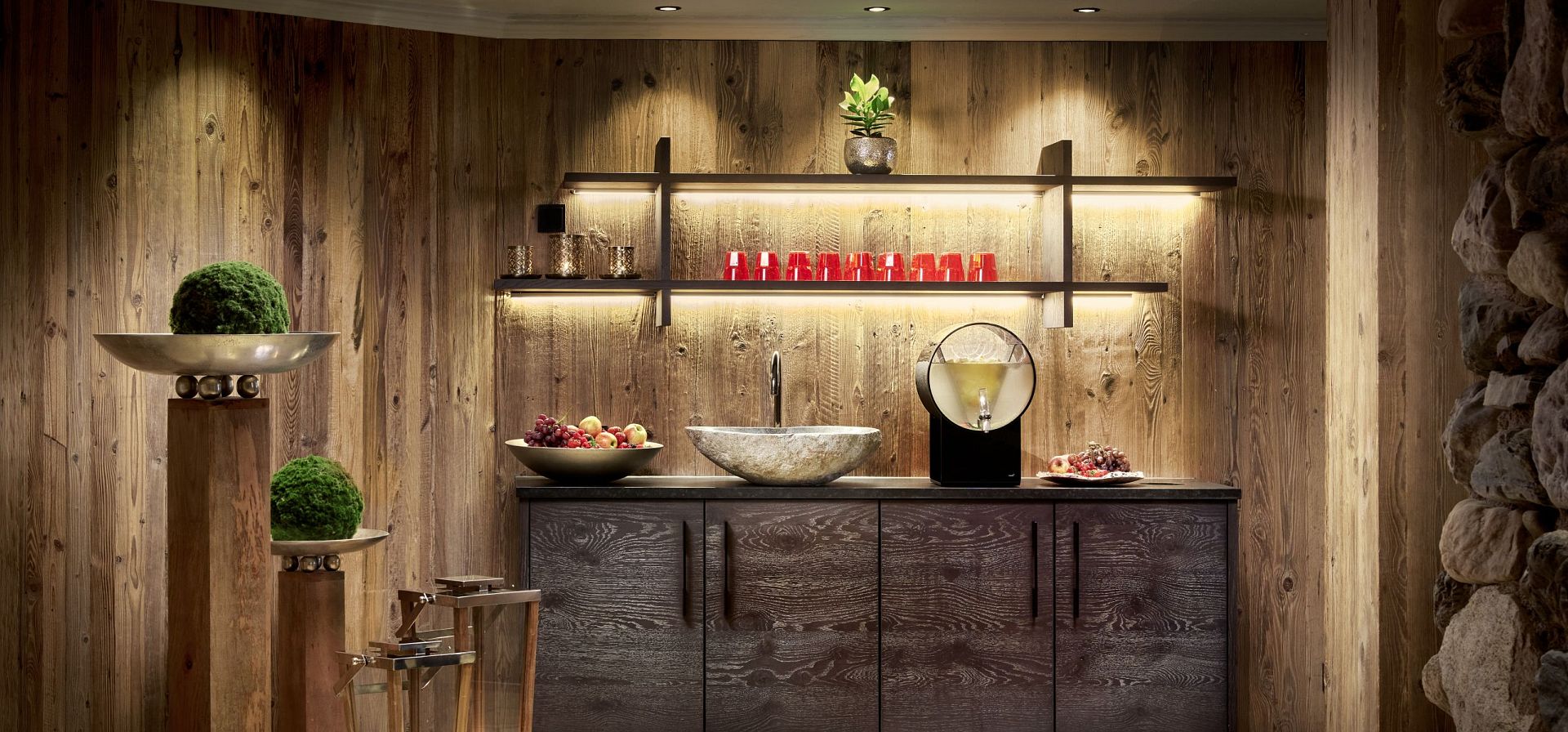 Gemütlicher Raum mit Holzverkleidung, modernen Regalen, Waschbecken und Dekorationen. Warm beleuchtet und einladend, perfekt für Entspannung.