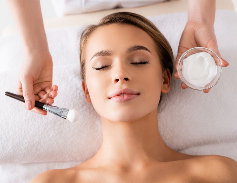 Entspannte Dame während einer Gesihtsbehandlung. Die Kosmetikerin hält einen Pinsel in der Hand.