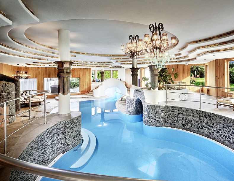 Ein luxuriöser Innenpool mit geschwungenen Formen, moderner Beleuchtung und eleganter Dekoration, ideal zum Entspannen. Die Fenster bieten Gartenblick.