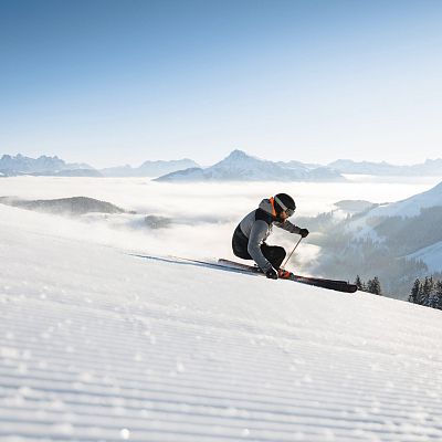 Carvender Skifahrer auf perfekt präparierten Pisten im Skigebiet Wilder Kaiser bei blauem Himmel und weißer Bergkulisse im Hintergrund