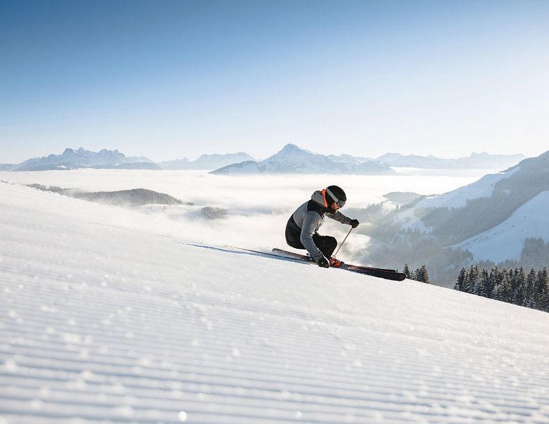 Carvender Skifahrer auf perfekt präparierten Pisten im Skigebiet Wilder Kaiser bei blauem Himmel und weißer Bergkulisse im Hintergrund